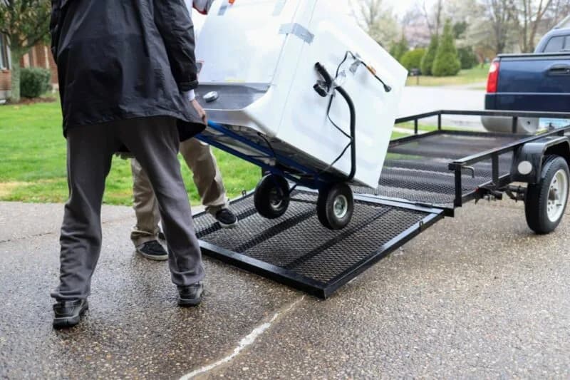 A washing machine on a hand truck being wheeled up a trailer ramp