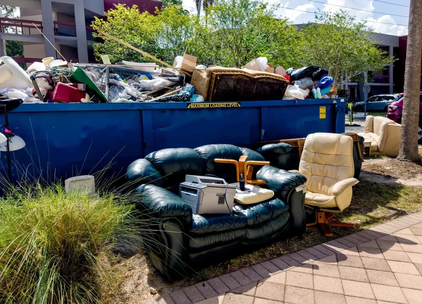 An old leather sofa and armchairs set out for removal beside a full container